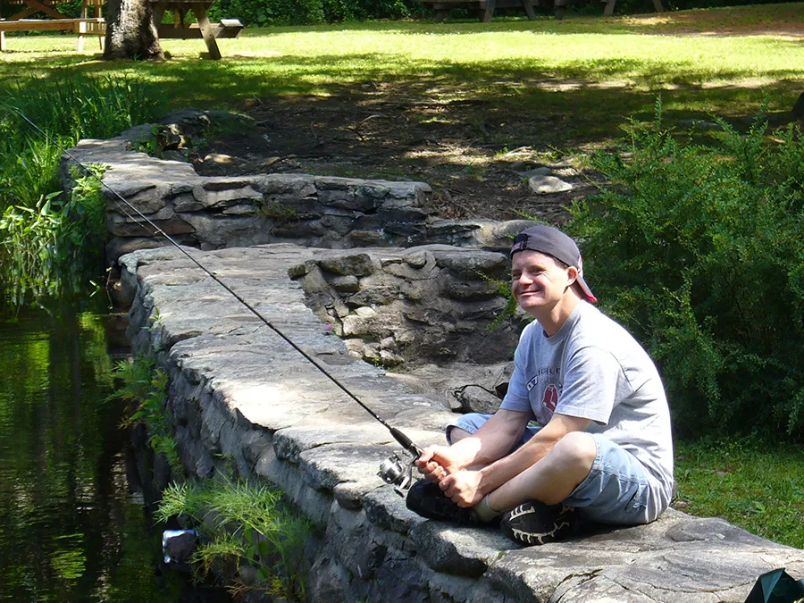 Man fishing while sitting on a stone wall